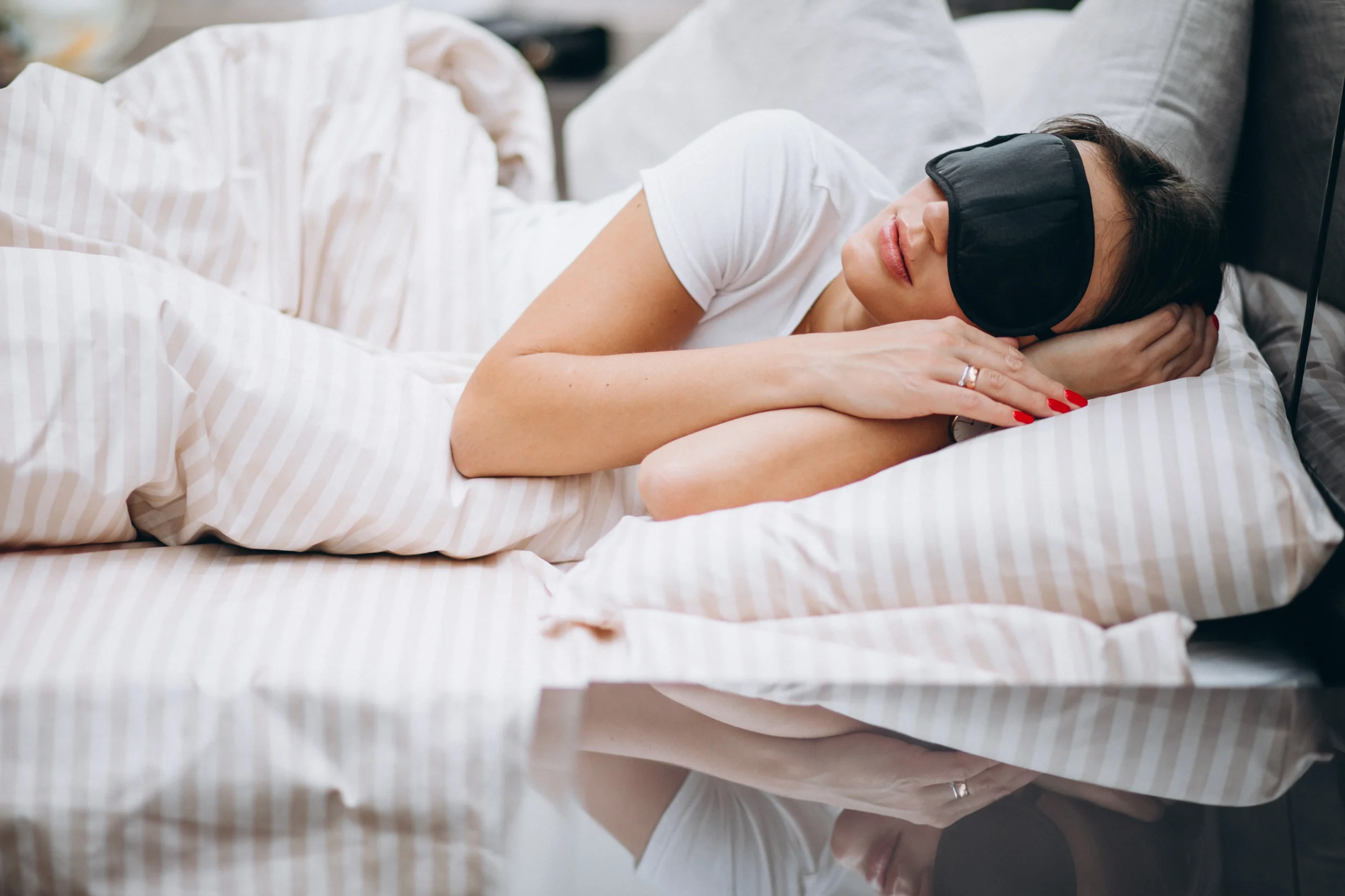 Woman resting peacefully under bed covers with eye mask